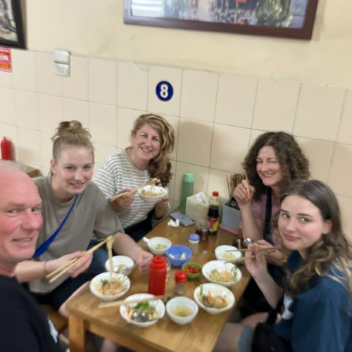 Five people enjoying a meal at a small, casual restaurant with bowls and chopsticks.