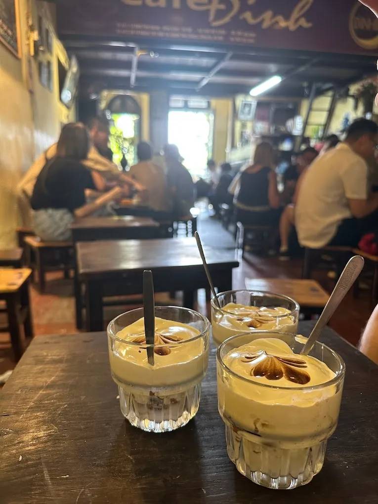 Three glasses of egg coffee with spoons on a table in a busy cafe.
