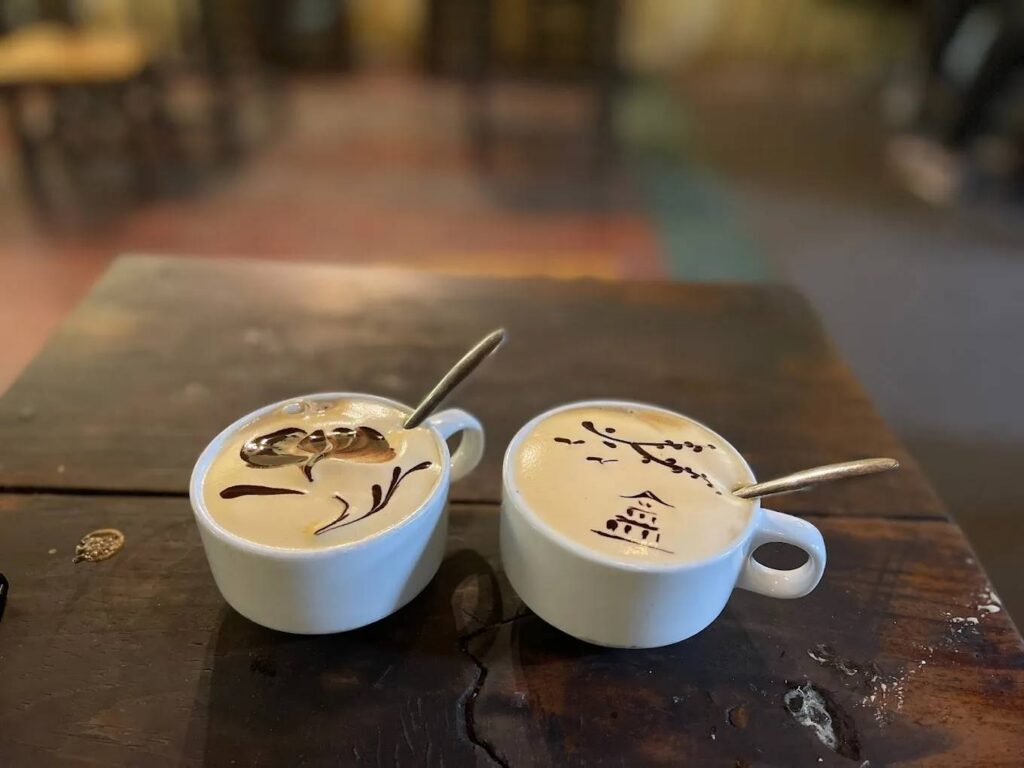 Two cups of coffee with artistic designs on a wooden table.