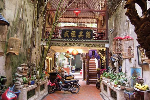 Courtyard with plants, scooters, and hanging cages under a traditional Asian balcony.