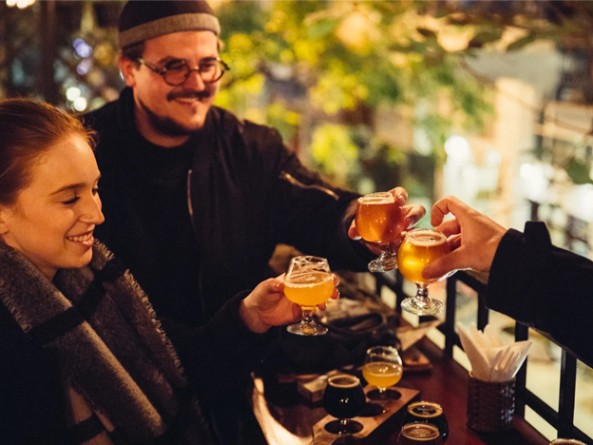 Three people toasting with beer glasses on an outdoor patio.