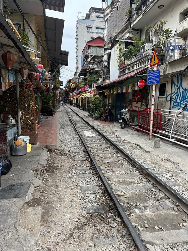 Narrow street with railway tracks between buildings and shops in an urban area.