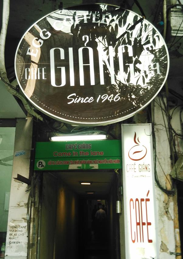 Entrance to Cafe Giang with a round sign above, narrow passageway.