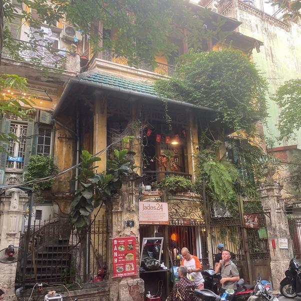 Street view of a cafe with plants, people, and motorcycles outside.