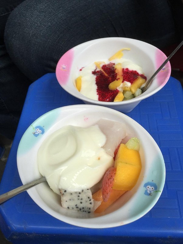 Two bowls of yogurt topped with mixed fruits on a blue surface.